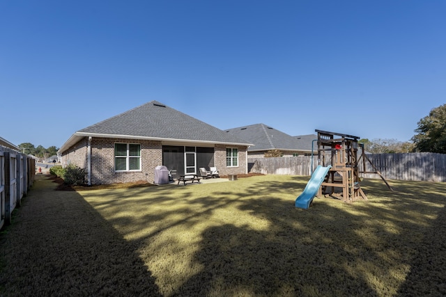 back of house with a lawn, a fenced backyard, a playground, roof with shingles, and brick siding