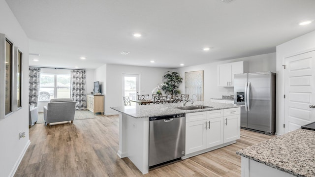 kitchen featuring light hardwood / wood-style flooring, appliances with stainless steel finishes, light stone countertops, white cabinets, and a center island with sink