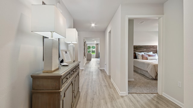 hall with light wood-style flooring, visible vents, and baseboards