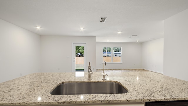 kitchen featuring light stone counters, open floor plan, and a sink