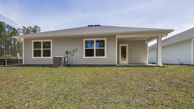 rear view of house with cooling unit, a shingled roof, and a yard