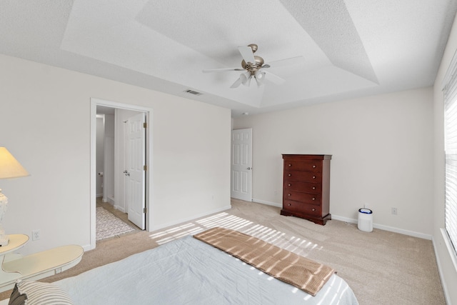 bedroom with ceiling fan, a raised ceiling, light carpet, and a textured ceiling