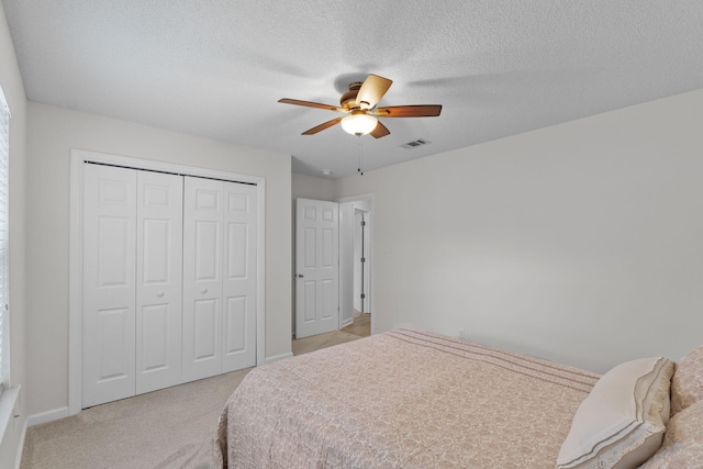 bedroom featuring ceiling fan, a closet, light carpet, and a textured ceiling