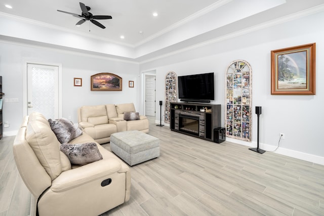 living room with a tray ceiling, ornamental molding, ceiling fan, and light wood-type flooring