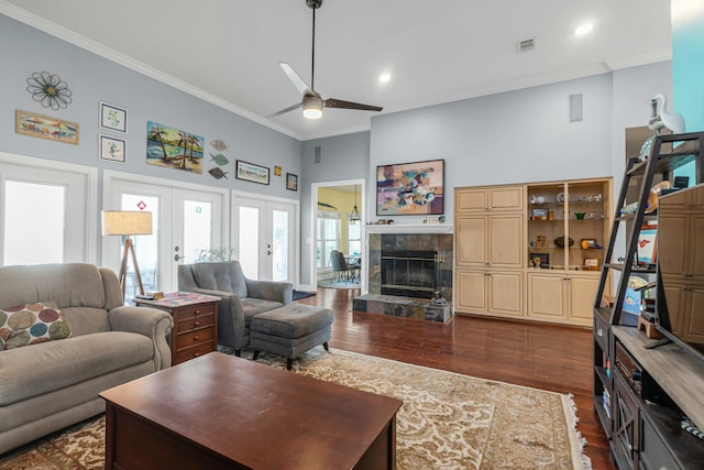 living room featuring crown molding, dark wood-type flooring, a tile fireplace, a towering ceiling, and french doors