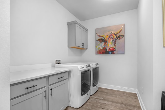 laundry area featuring light wood-type flooring, washing machine and clothes dryer, cabinet space, and baseboards