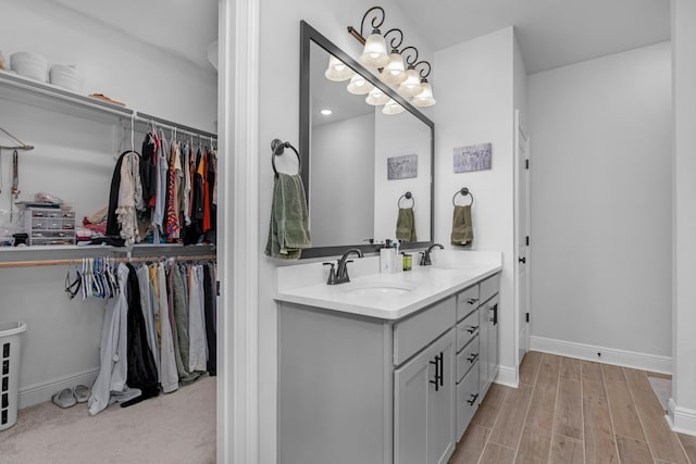 bathroom with a sink, wood finished floors, baseboards, double vanity, and a walk in closet