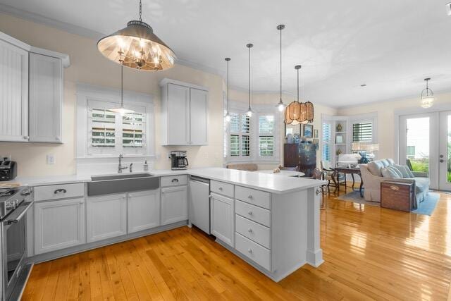 kitchen with sink, stainless steel appliances, light hardwood / wood-style floors, decorative light fixtures, and kitchen peninsula