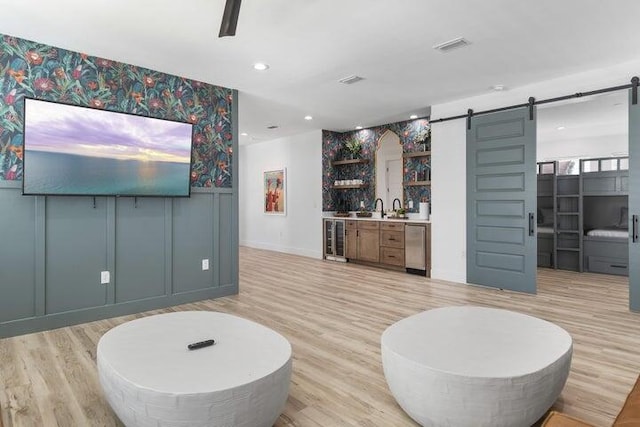 living room with beverage cooler, a barn door, light hardwood / wood-style floors, and indoor wet bar