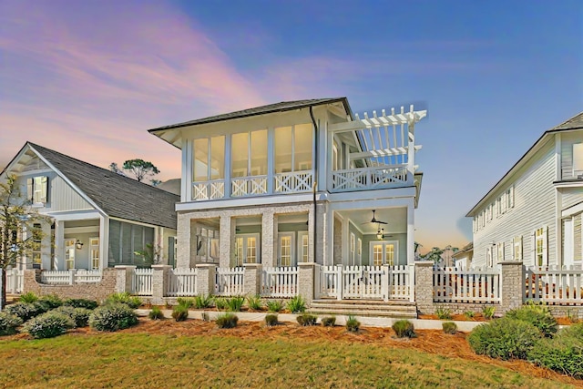 back house at dusk with a balcony, ceiling fan, and a lawn