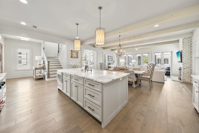 kitchen featuring white cabinetry, light stone counters, wood-type flooring, decorative light fixtures, and a kitchen island