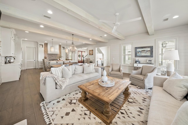 living room with dark wood-type flooring, beam ceiling, and ceiling fan with notable chandelier