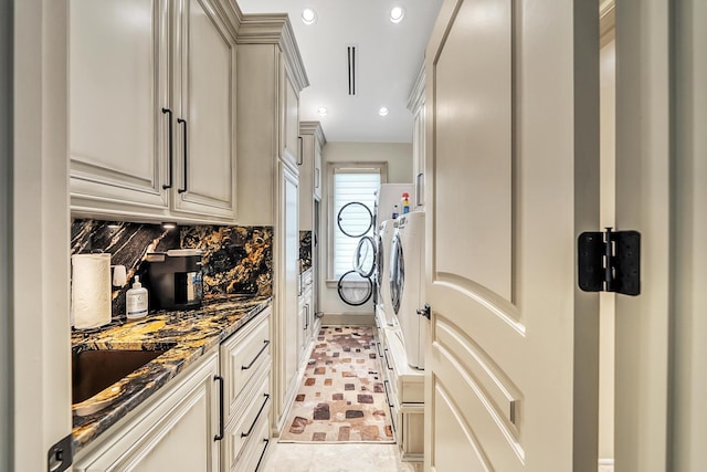 kitchen featuring dark stone countertops, decorative backsplash, washer and clothes dryer, and cream cabinetry