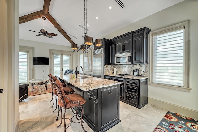 kitchen featuring appliances with stainless steel finishes, pendant lighting, sink, a kitchen bar, and a center island with sink