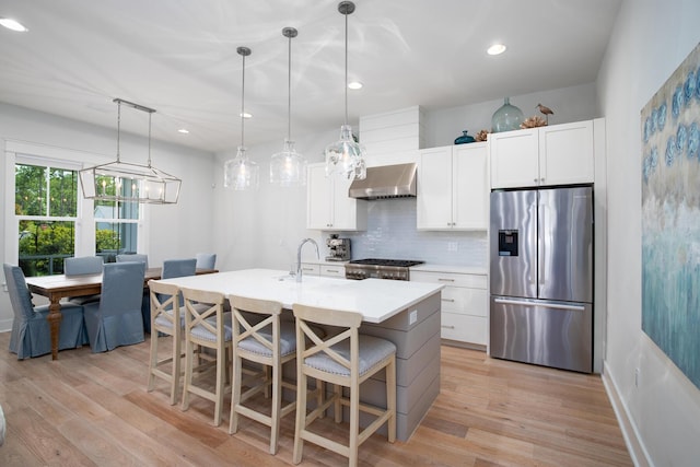 kitchen with light wood-type flooring, decorative backsplash, range hood, stainless steel refrigerator with ice dispenser, and range