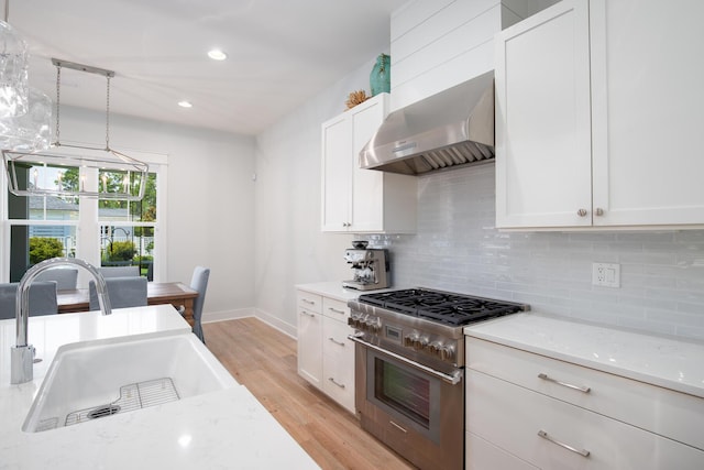 kitchen featuring light wood-type flooring, high end stove, a sink, wall chimney range hood, and decorative backsplash