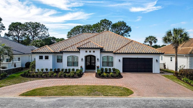 mediterranean / spanish-style home featuring driveway, a tiled roof, an attached garage, and stucco siding