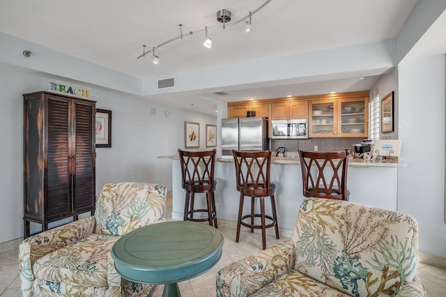 interior space with appliances with stainless steel finishes, kitchen peninsula, decorative backsplash, and light tile patterned floors