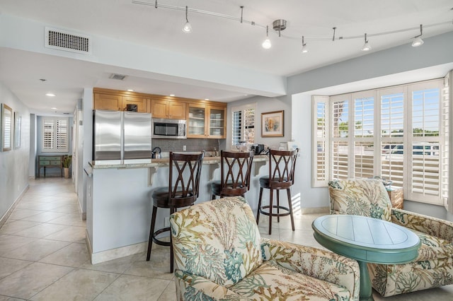 kitchen featuring appliances with stainless steel finishes, a breakfast bar, backsplash, light tile patterned floors, and light stone countertops