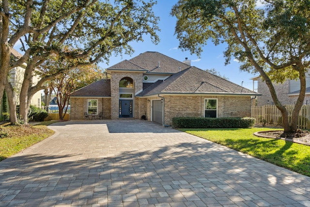 view of front of property featuring decorative driveway, a chimney, fence, a garage, and a front lawn