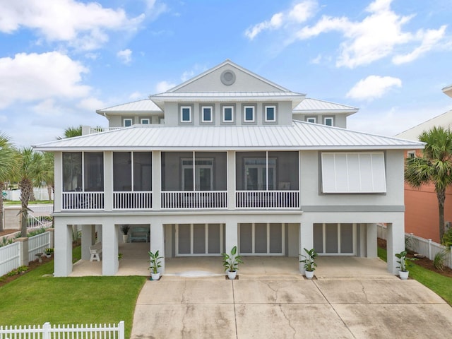 raised beach house featuring a sunroom, driveway, a carport, a standing seam roof, and a front yard