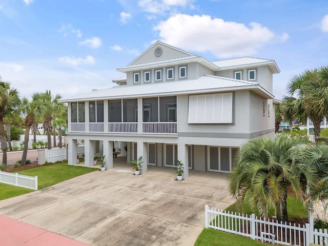 raised beach house with concrete driveway, a sunroom, metal roof, fence private yard, and a carport