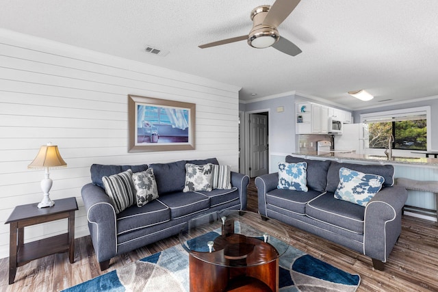 living room with dark wood-type flooring, sink, crown molding, a textured ceiling, and ceiling fan