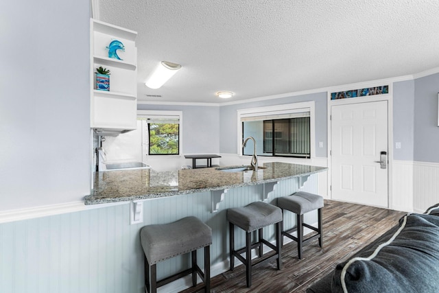 kitchen with sink, dark wood-type flooring, a kitchen breakfast bar, light stone counters, and kitchen peninsula