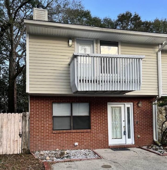 view of front of house with a chimney, brick siding, fence, and a balcony