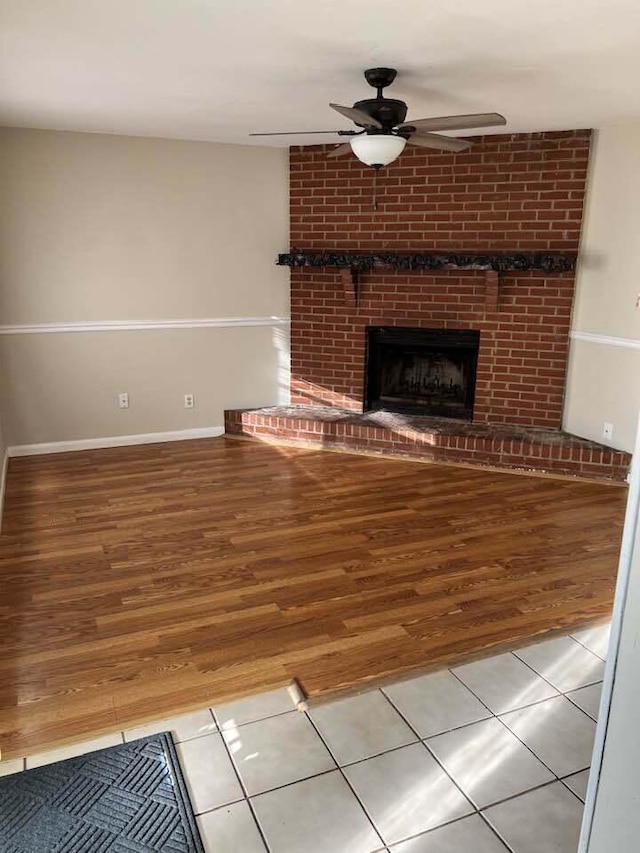 unfurnished living room with ceiling fan, a fireplace, baseboards, and wood finished floors