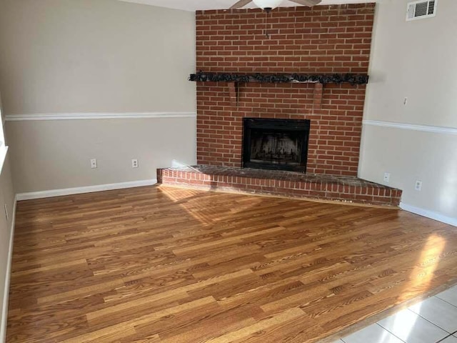 unfurnished living room featuring a brick fireplace, visible vents, baseboards, and wood finished floors