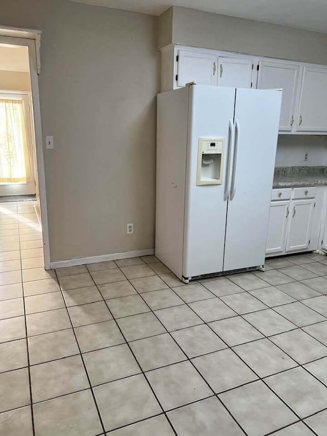 kitchen featuring light tile patterned floors, white fridge with ice dispenser, baseboards, and white cabinets