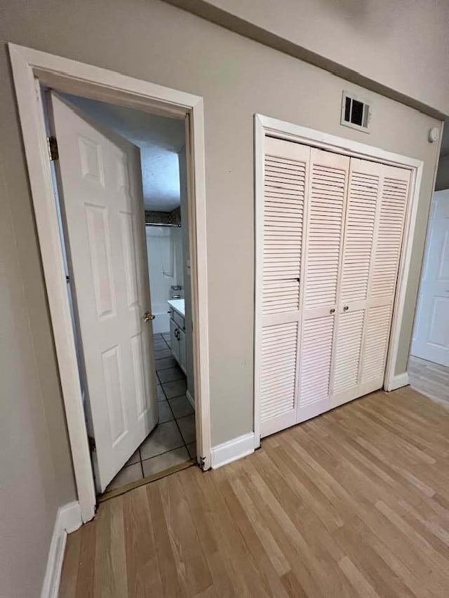 unfurnished bedroom featuring connected bathroom, visible vents, baseboards, light wood-style floors, and a closet