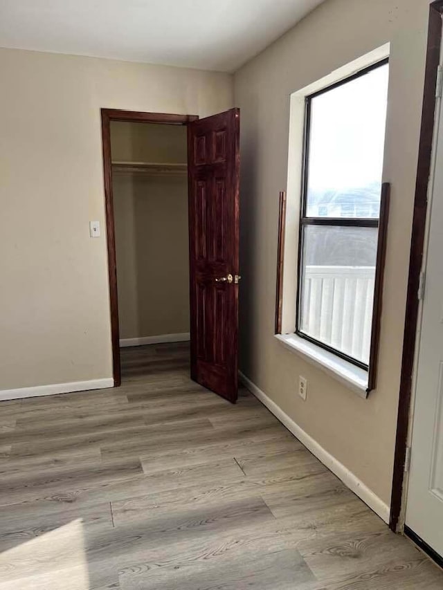 unfurnished bedroom featuring light wood-type flooring, baseboards, and a closet