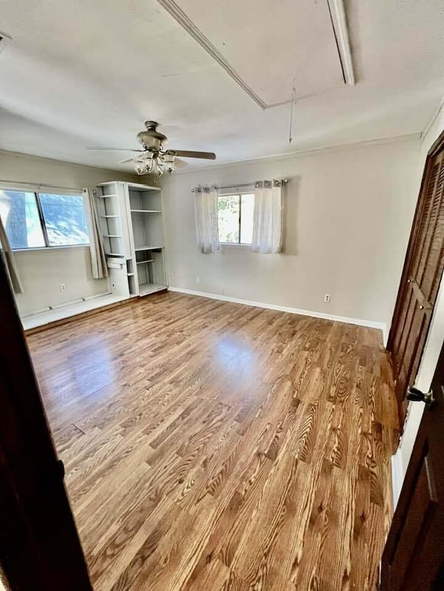 unfurnished bedroom featuring multiple windows, wood finished floors, attic access, and baseboards