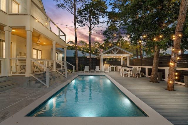 pool at dusk featuring a wooden deck and a gazebo