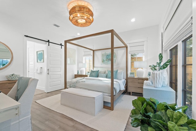 bedroom featuring multiple windows, a barn door, and light hardwood / wood-style floors