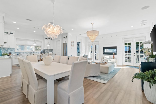 dining space featuring french doors, sink, light wood-type flooring, and a notable chandelier