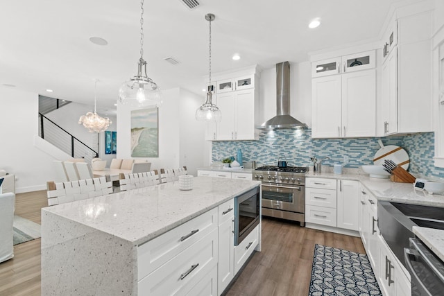 kitchen with a kitchen island, appliances with stainless steel finishes, white cabinetry, hanging light fixtures, and wall chimney exhaust hood