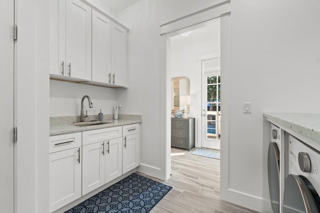 interior space featuring white cabinetry, sink, washer / dryer, and light stone counters