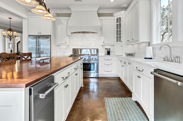 kitchen featuring sink, white cabinetry, hanging light fixtures, premium appliances, and custom range hood