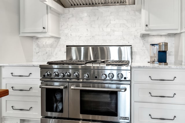 kitchen with backsplash, double oven range, light stone countertops, and white cabinets