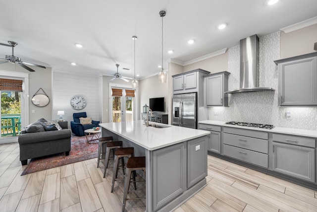 kitchen featuring wall chimney range hood, gray cabinets, a breakfast bar area, appliances with stainless steel finishes, and a kitchen island with sink