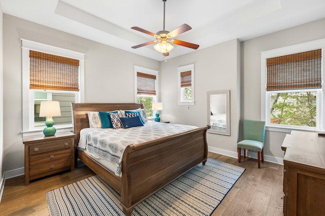 bedroom with ceiling fan, a raised ceiling, and light hardwood / wood-style floors