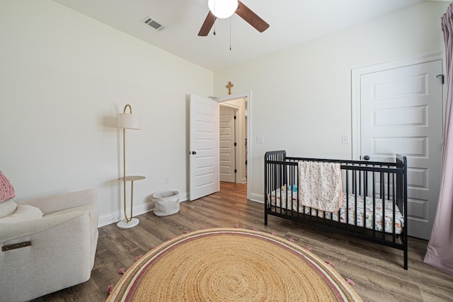 bedroom with visible vents, a crib, baseboards, wood finished floors, and a ceiling fan