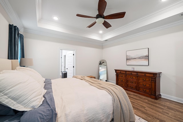 bedroom featuring baseboards, a raised ceiling, wood finished floors, and crown molding