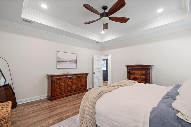 bedroom featuring visible vents, ornamental molding, a tray ceiling, wood finished floors, and baseboards