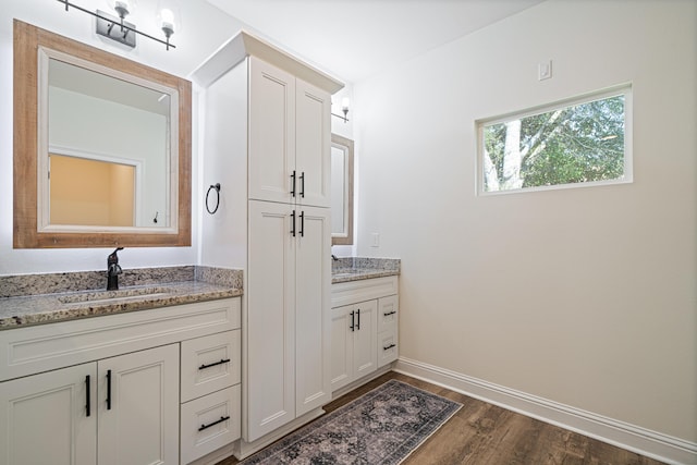 bathroom featuring a sink, baseboards, two vanities, and wood finished floors