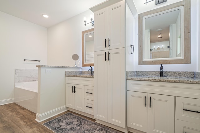 full bath featuring wood finished floors, baseboards, two vanities, a sink, and a bath