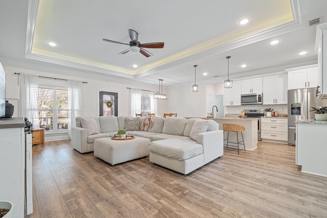 living area with visible vents, a healthy amount of sunlight, light wood-style floors, and a tray ceiling